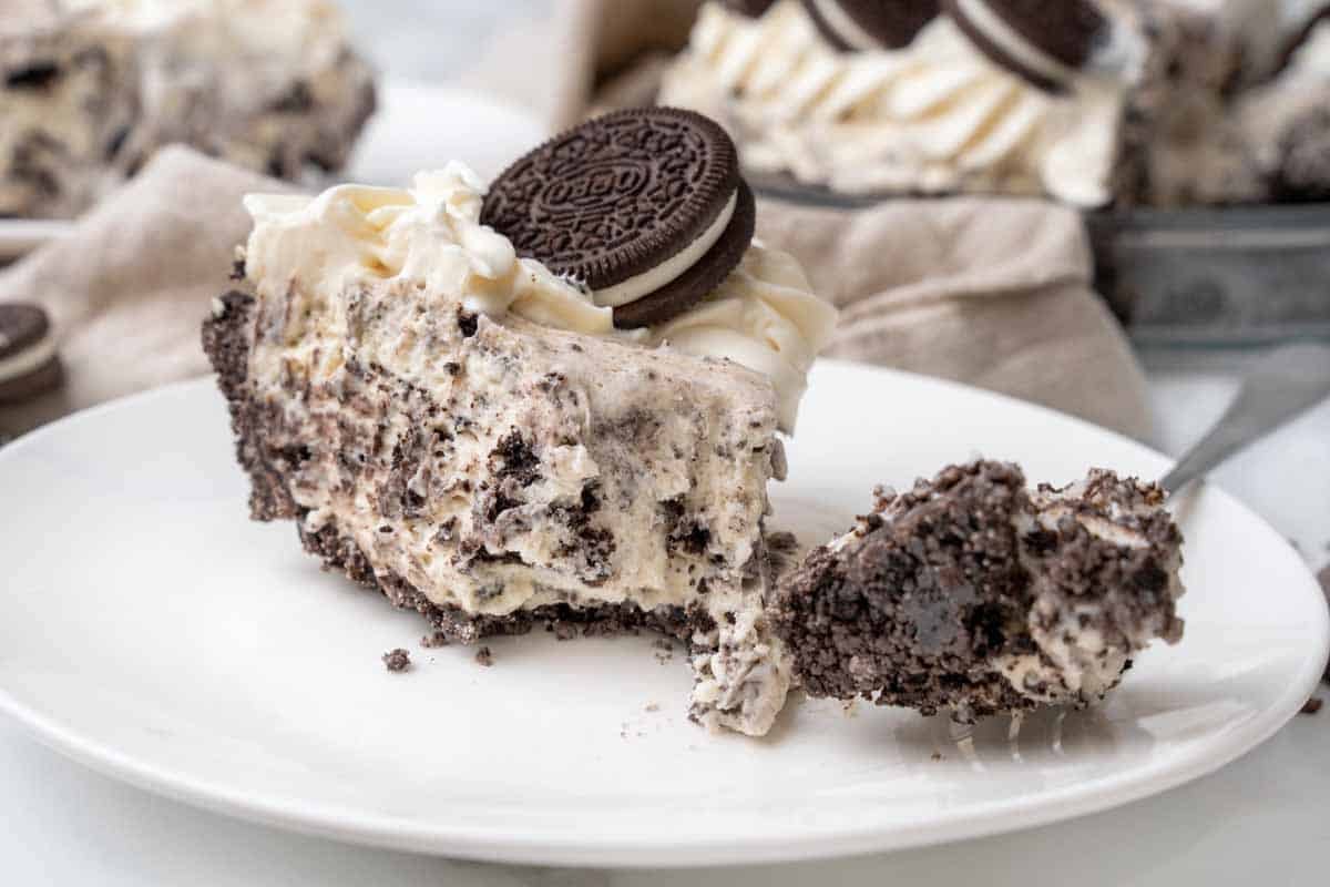 Slice of an oreo pie with a forkful taken out on a white plate.