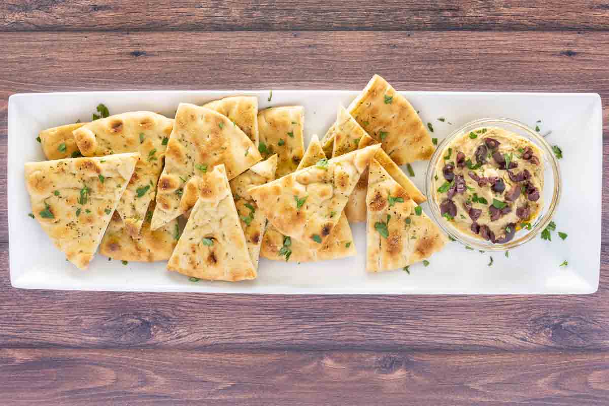 Pita chips on a white oblong platter with hummus.