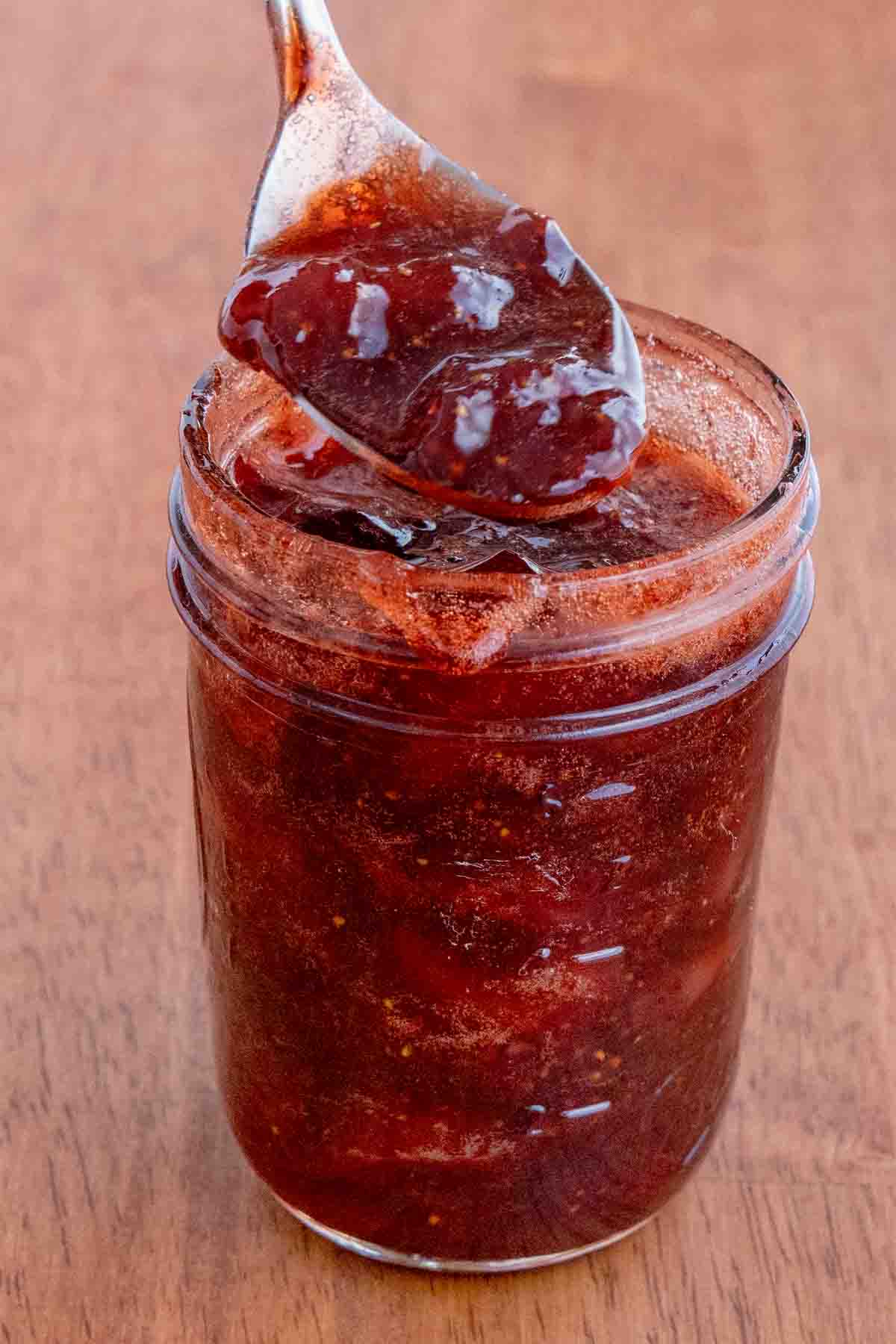 Strawberry Jam in a glass jar with a spoon coming out.