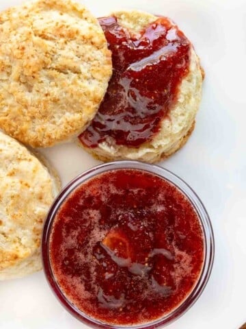 Strawberry jam and biscuits on a white plate.
