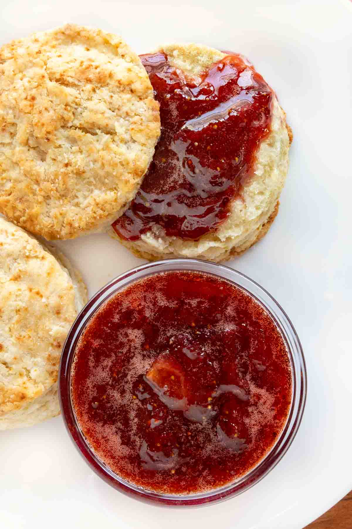 Strawberry jam and biscuits on a white plate.
