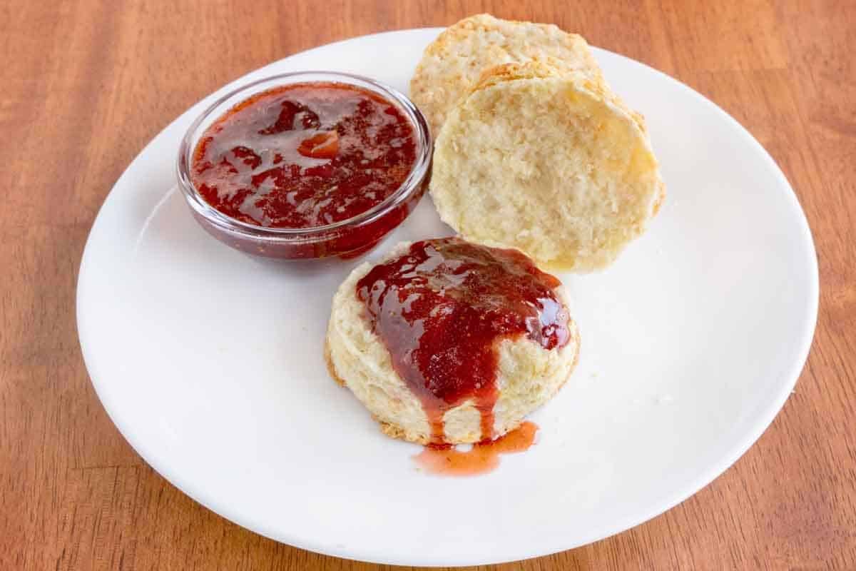 Strawberry jam and biscuits on a white plate.