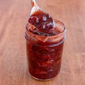 Strawberry Jam in a glass jar with a spoon coming out.