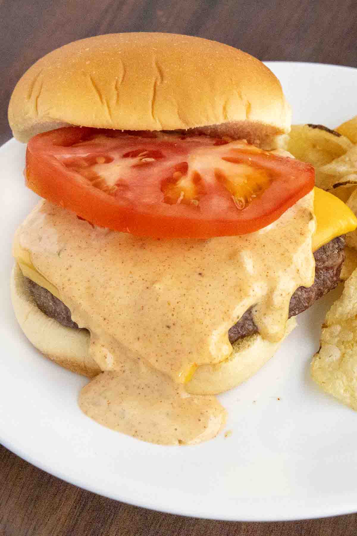 Cheeseburger with big mac sauce and a slice of tomato on a white plate.