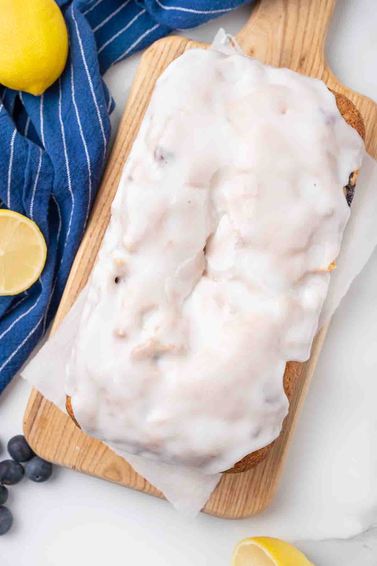 Loaf of blueberry bread with lemon icing on a wooden cutting board.