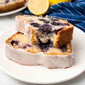 Two slices of blueberry bread, one with a piece missing on a white plate.