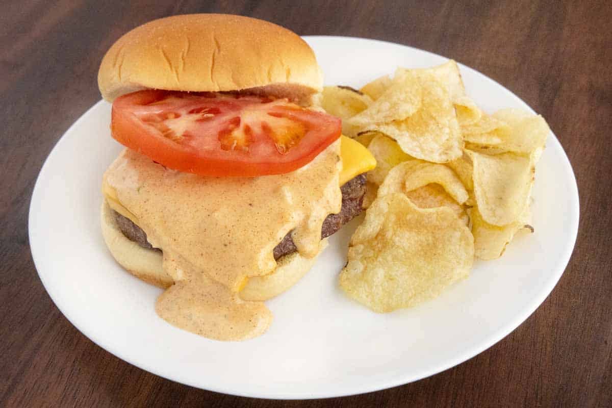 Cheeseburger with big mac sauce and a slice of tomato on a white plate.