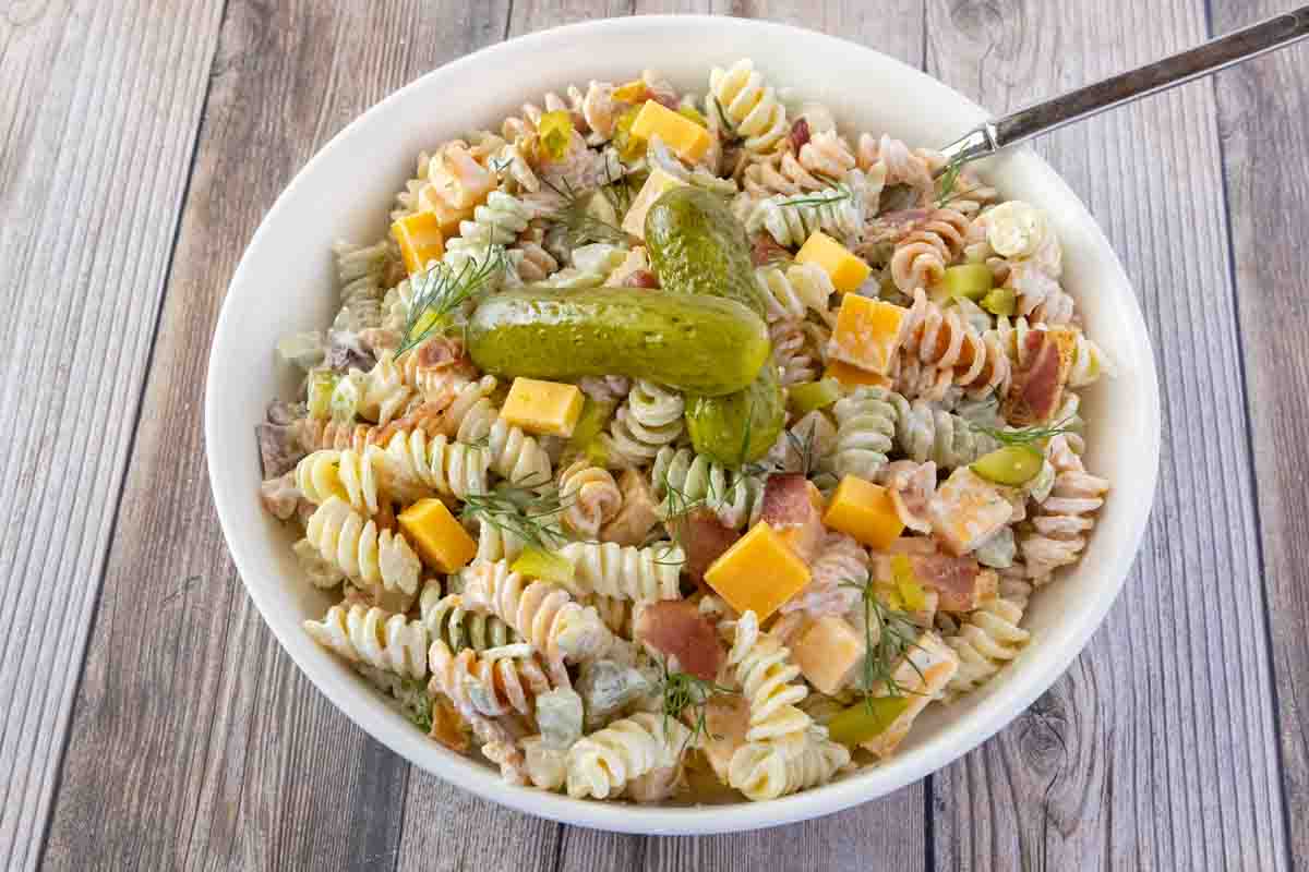 Dill pickles pasta salad in a white bowl with a spoon.