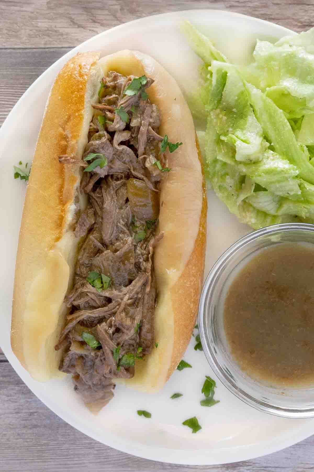 French dip sandwich on a white plate with au jus and salad.