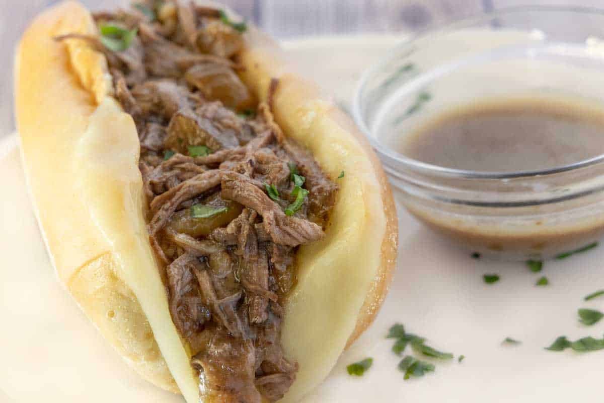 French dip sandwich on a white plate with au jus.