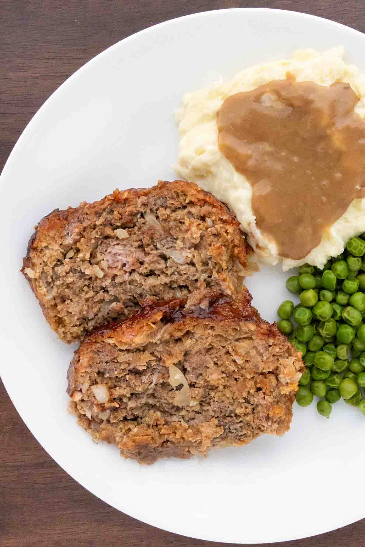 2 slices of Lipton French onion meatloaf with mashed potatoes and peas on a white plate.
