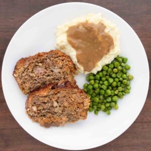 2 slices of Lipton French onion meatloaf with mashed potatoes and peas on a white plate.