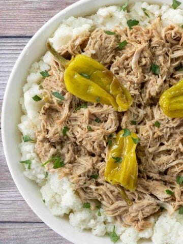 Slow Cooker Mississippi chicken on a bed of mashed potatoes in a white bowl.
