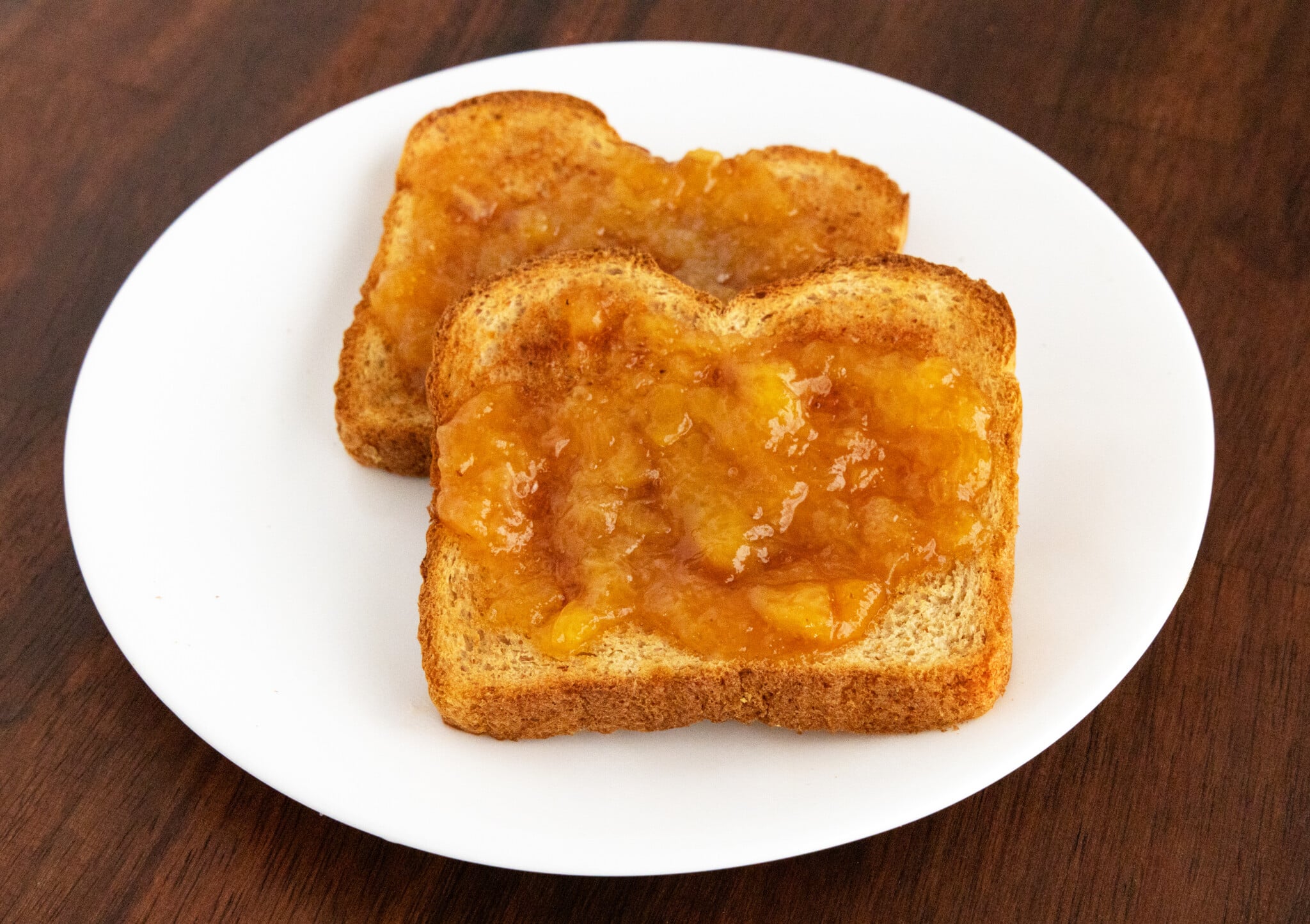 Peach Jam on toast on a white plate.