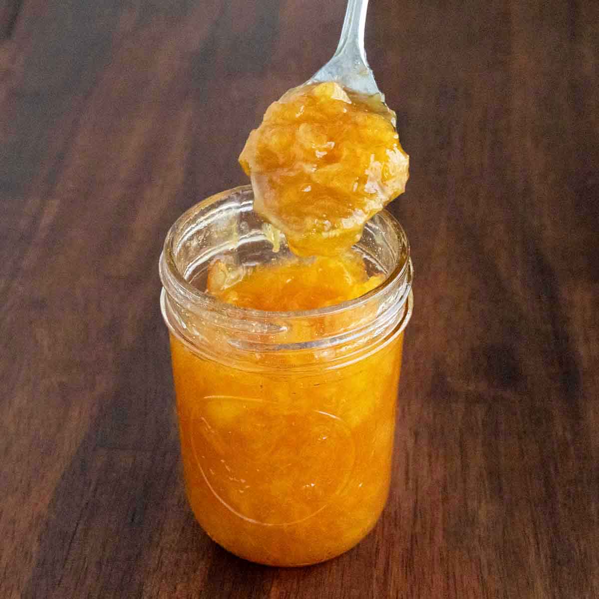 Peach Jam in a glass jar with a spoon coming out.