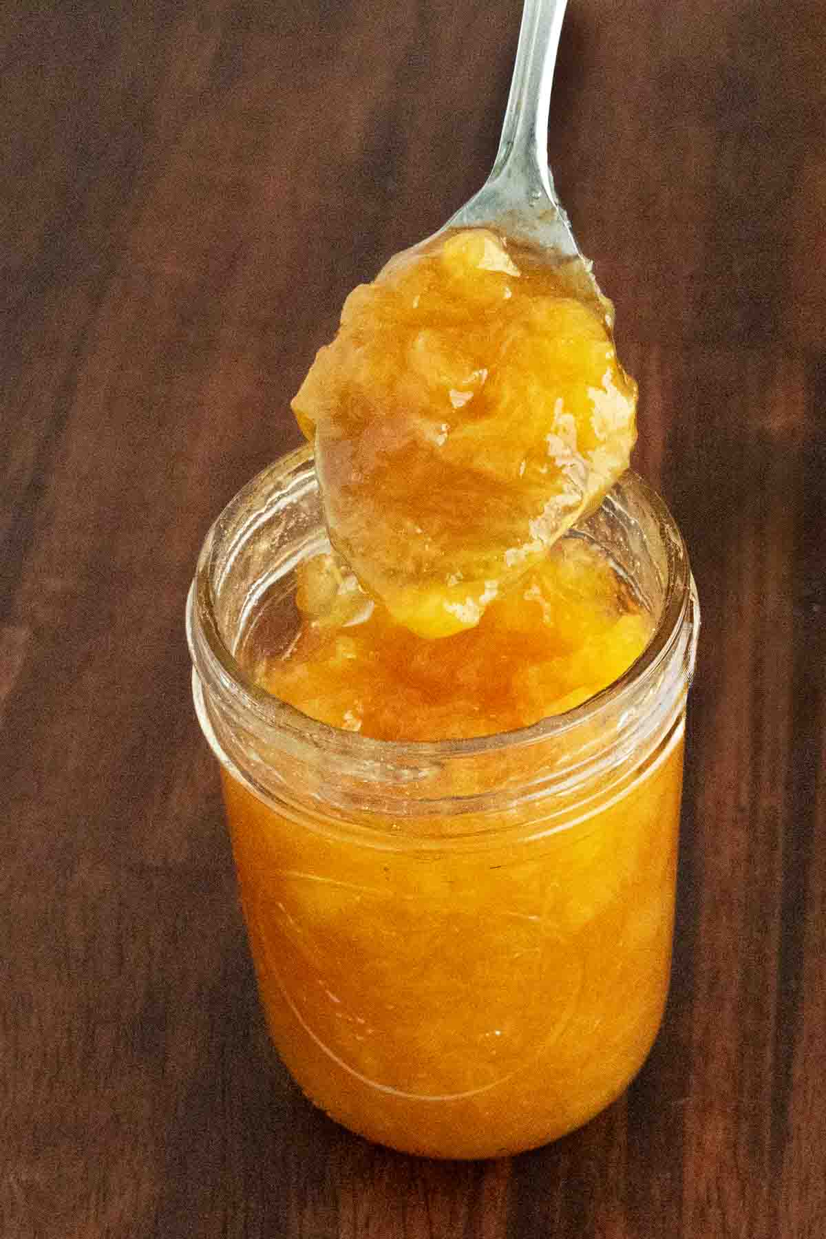 Peach Jam in a glass jar with a spoon coming out.