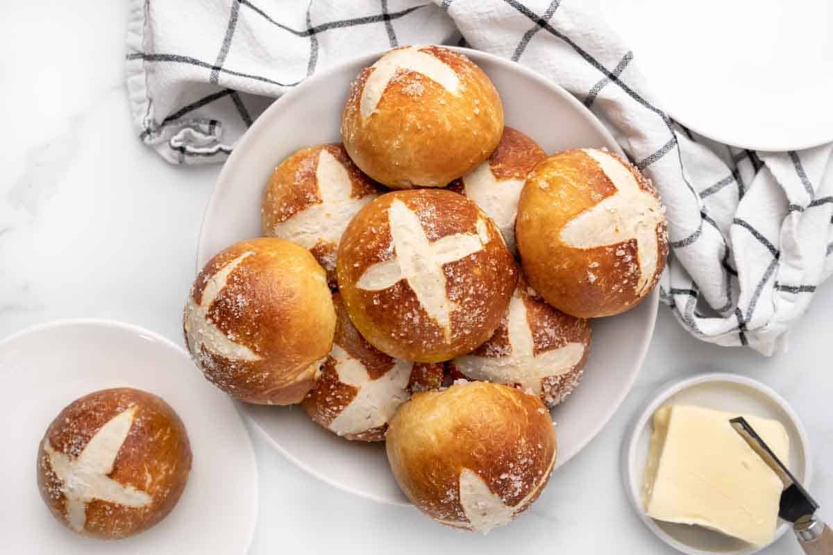 Pretzels rolls stacked on a white platter.