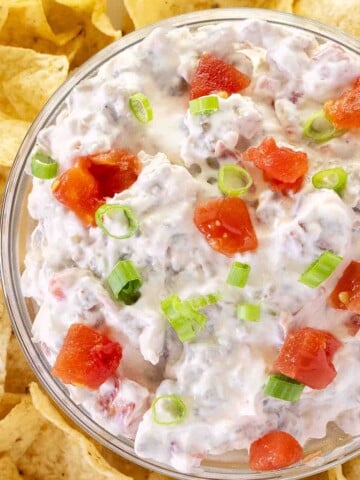 Rotel dip in a glass bowl on a platter with corn chips.