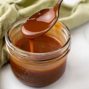 Caramel Sauce in a glass jar with a spoon coming out.