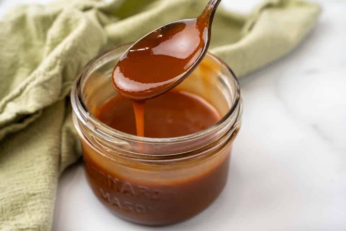 Caramel Sauce in a glass jar with a spoon coming out.