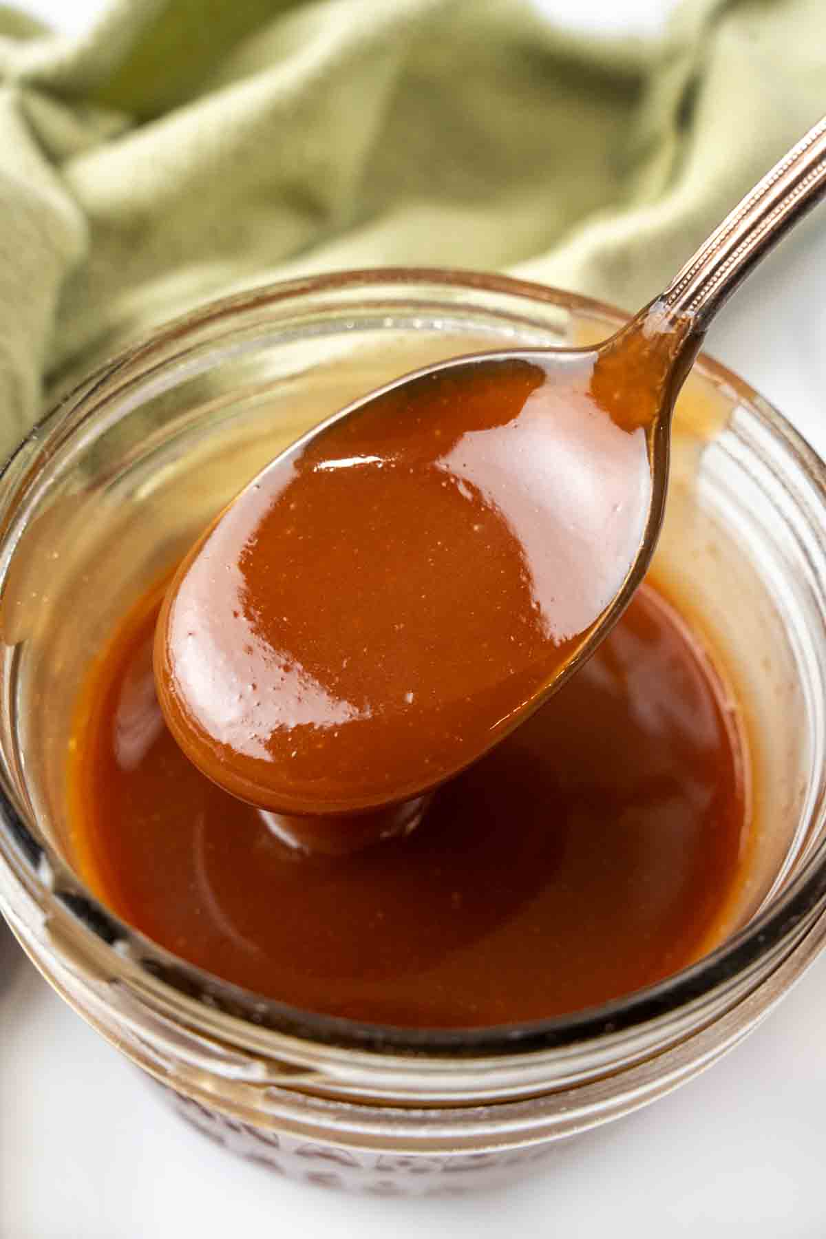 Caramel Sauce in a glass jar with a spoon coming out.