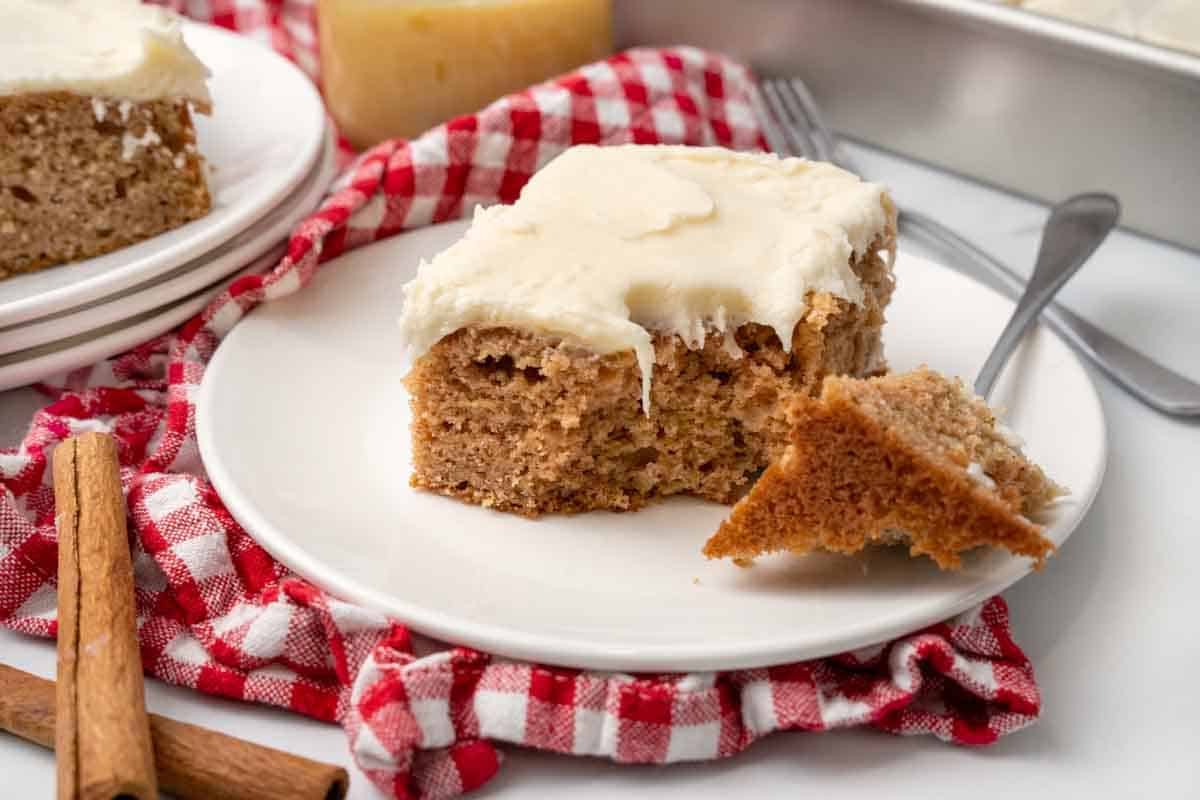 Applesauce cake on a white plate with a piece taken out with a fork.