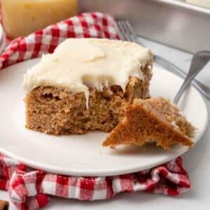Applesauce cake on a white plate with a piece taken out with a fork.