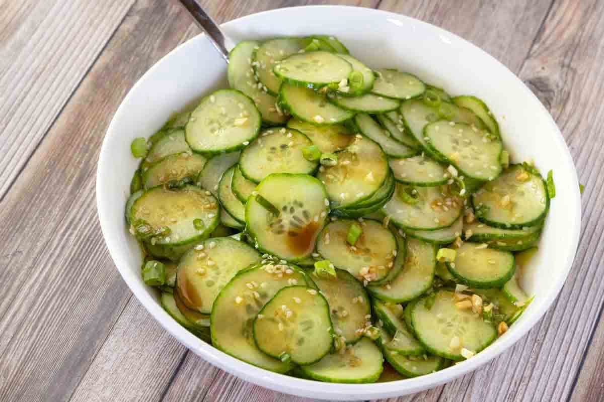 Asian cucumber salad in a white bowl with a spoon in it.