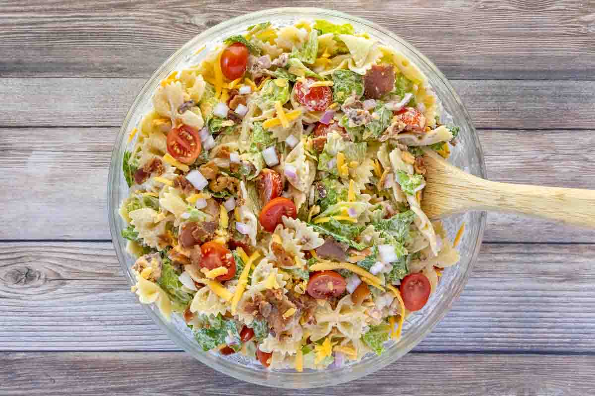 BLT pasta salad in a glass bowl with a wooden spoon.