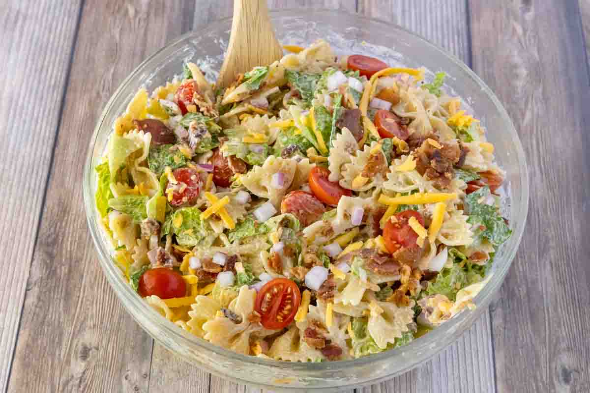 BLT pasta salad in a glass bowl with a wooden spoon.
