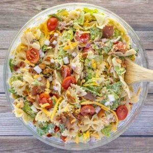 BLT pasta salad in a glass bowl with a wooden spoon.