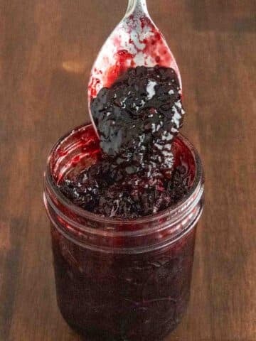 Blackberry jam in a glass jar with a spoon coming out.