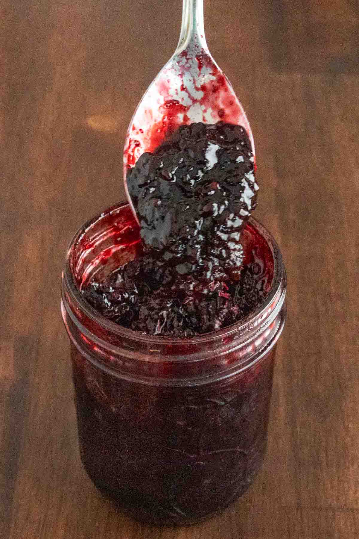 Blackberry jam in a glass jar with a spoon coming out.