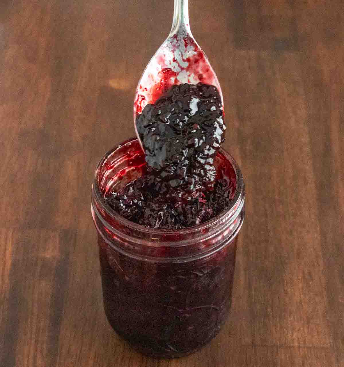 Blackberry jam in a glass jar with a spoon coming out.