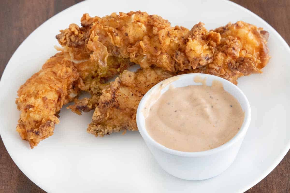 Cane's chicken sauce in a ramekin with fried chicken tenders on a white plate.