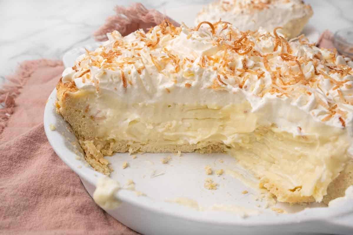 coconut cream pie in a white ple plate with slices taken out.