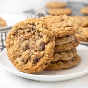 Stack of cowboy cookies, with one tipped over on a white plate.