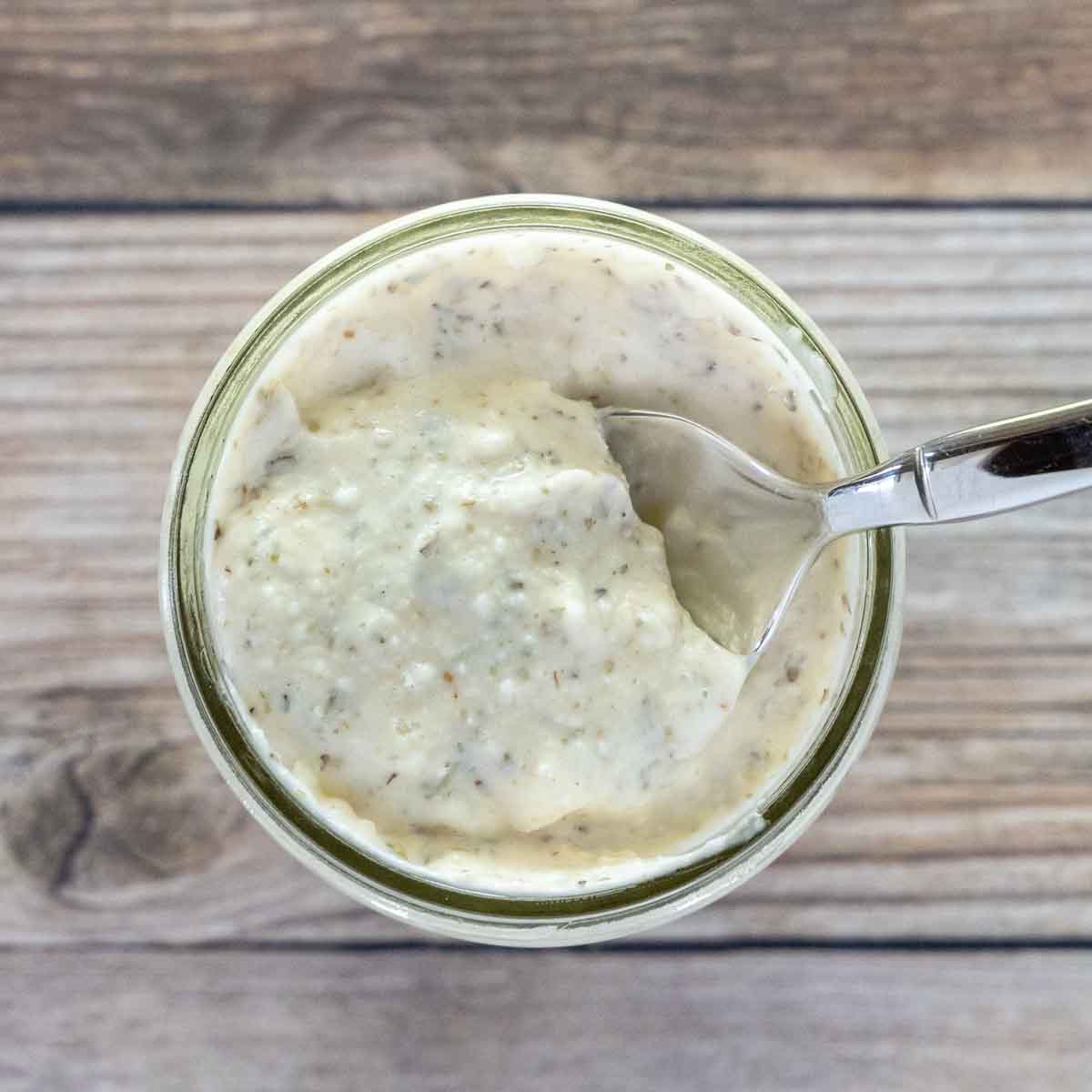 Creamy Italian dressing in a glass jar with a spoon in it.