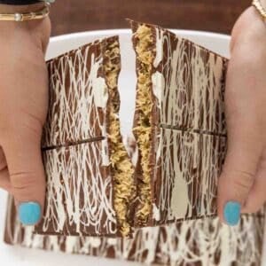 Two hands cracking Dubai Chocolate Bars over a white platter.