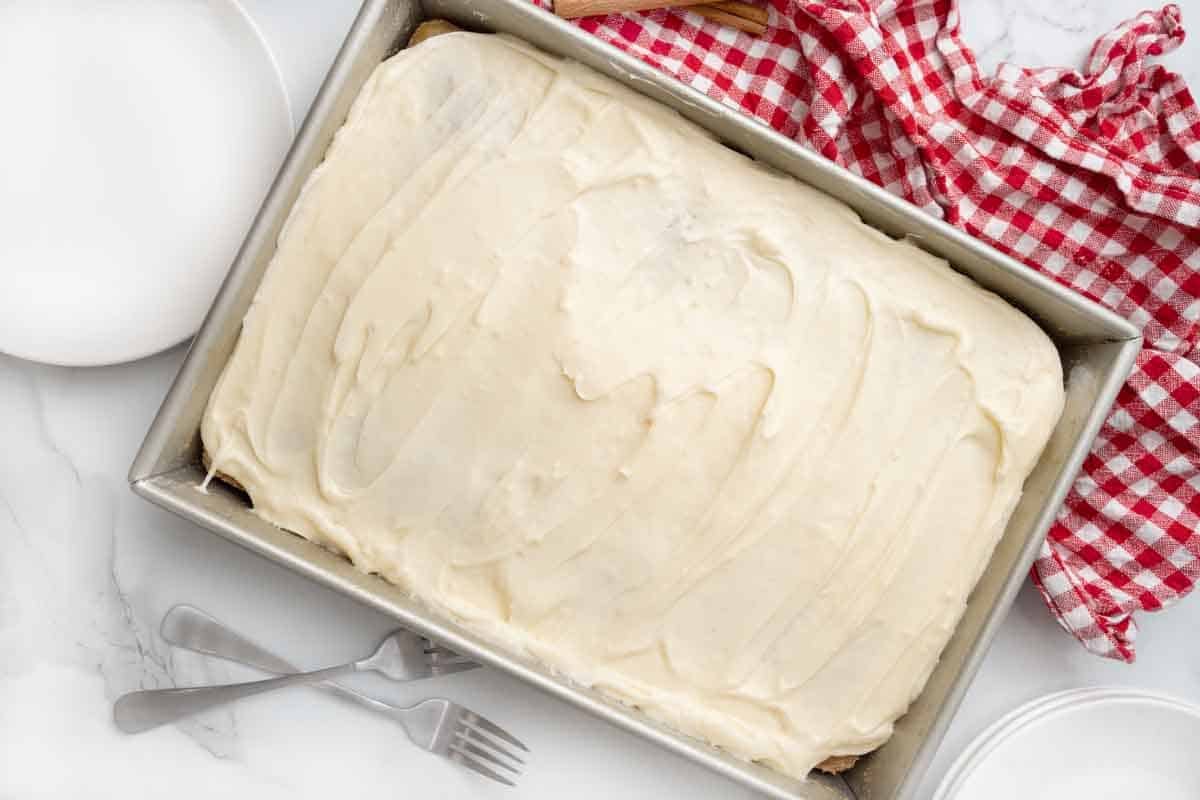 Frosted applesauce cake in the pan next to a red and white checked napkin.