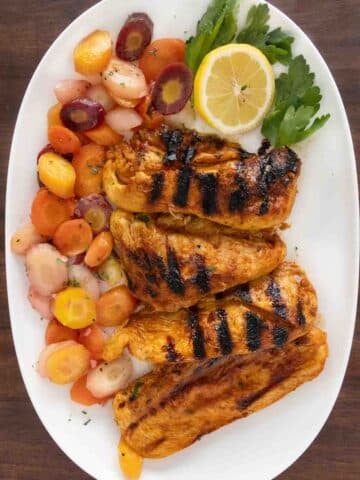 Harissa chicken with rainbow carrots on a white platter.