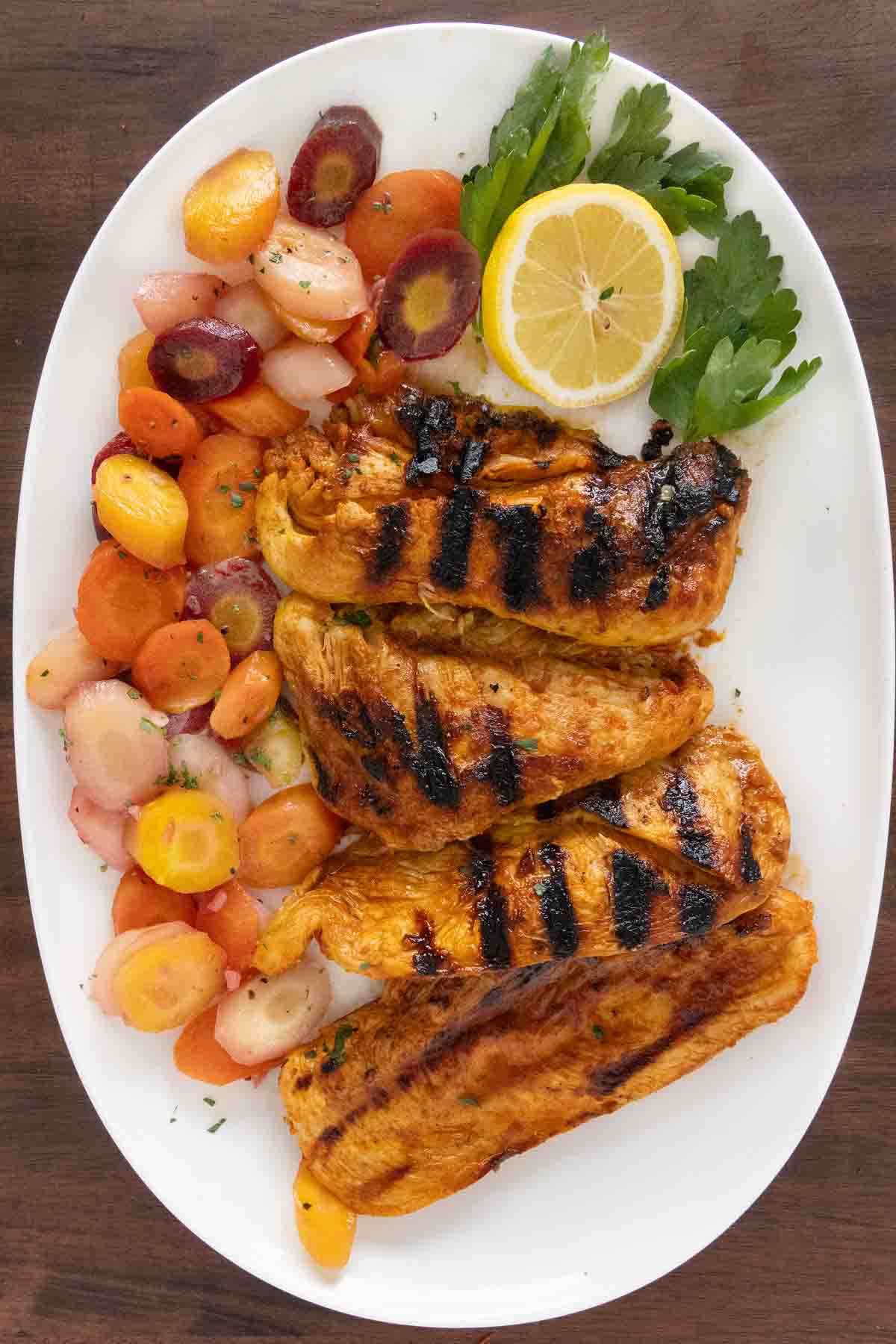 Harissa chicken with rainbow carrots on a white platter.