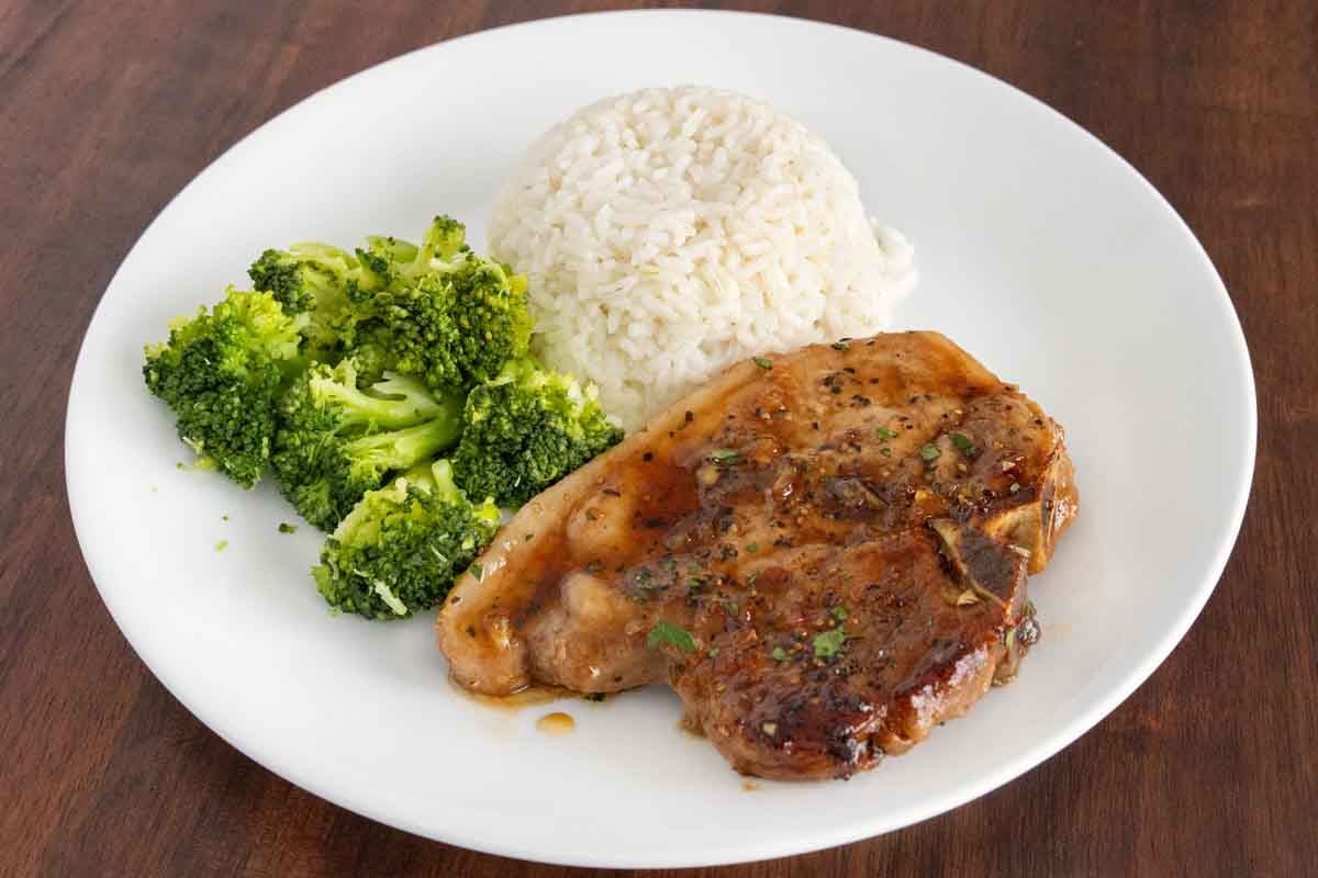 Honey garlic pork chops with rice and broccoli on a white plate.