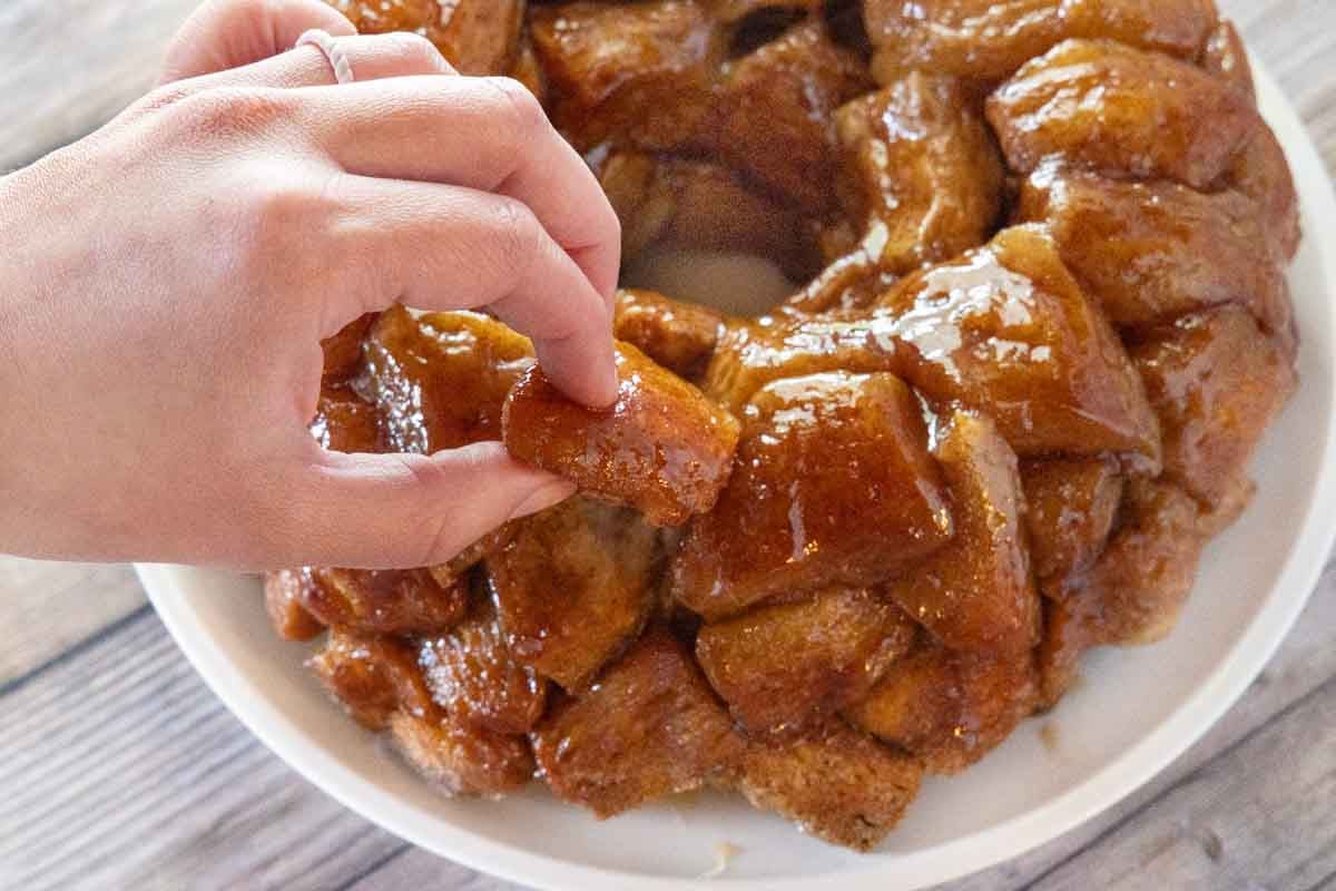 Hand taking a piece of monkey bread from the whole cake.