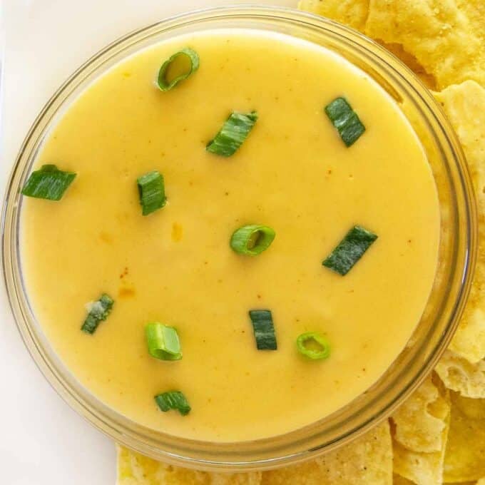 Bowl of queso dip on a white platter with tortilla chips.