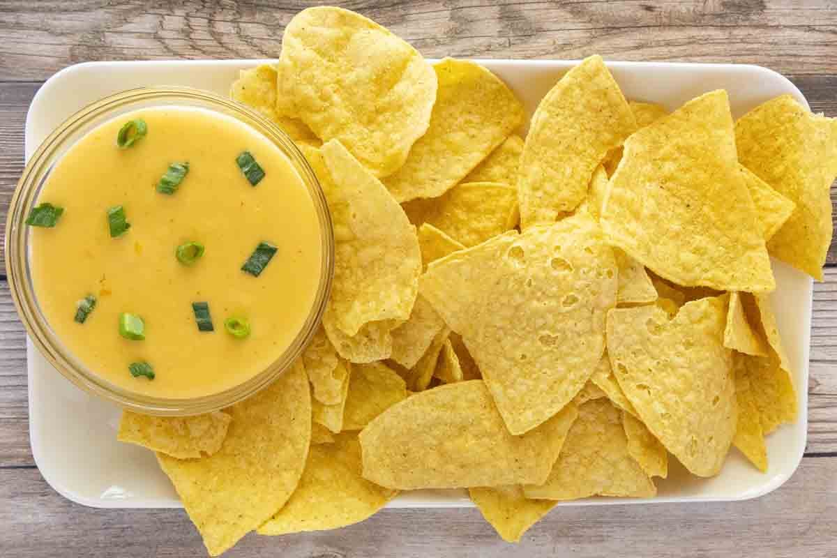 Bowl of queso dip on a white platter with tortilla chips.