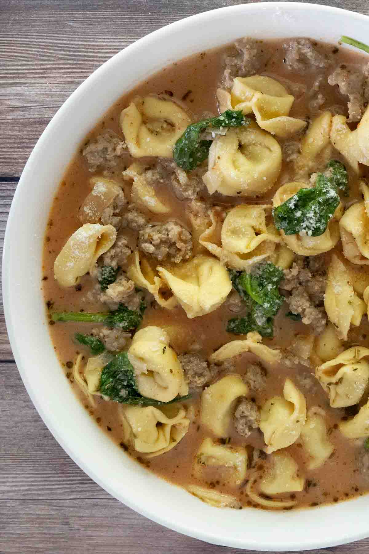 Sausage tortellini soup in a white bowl.