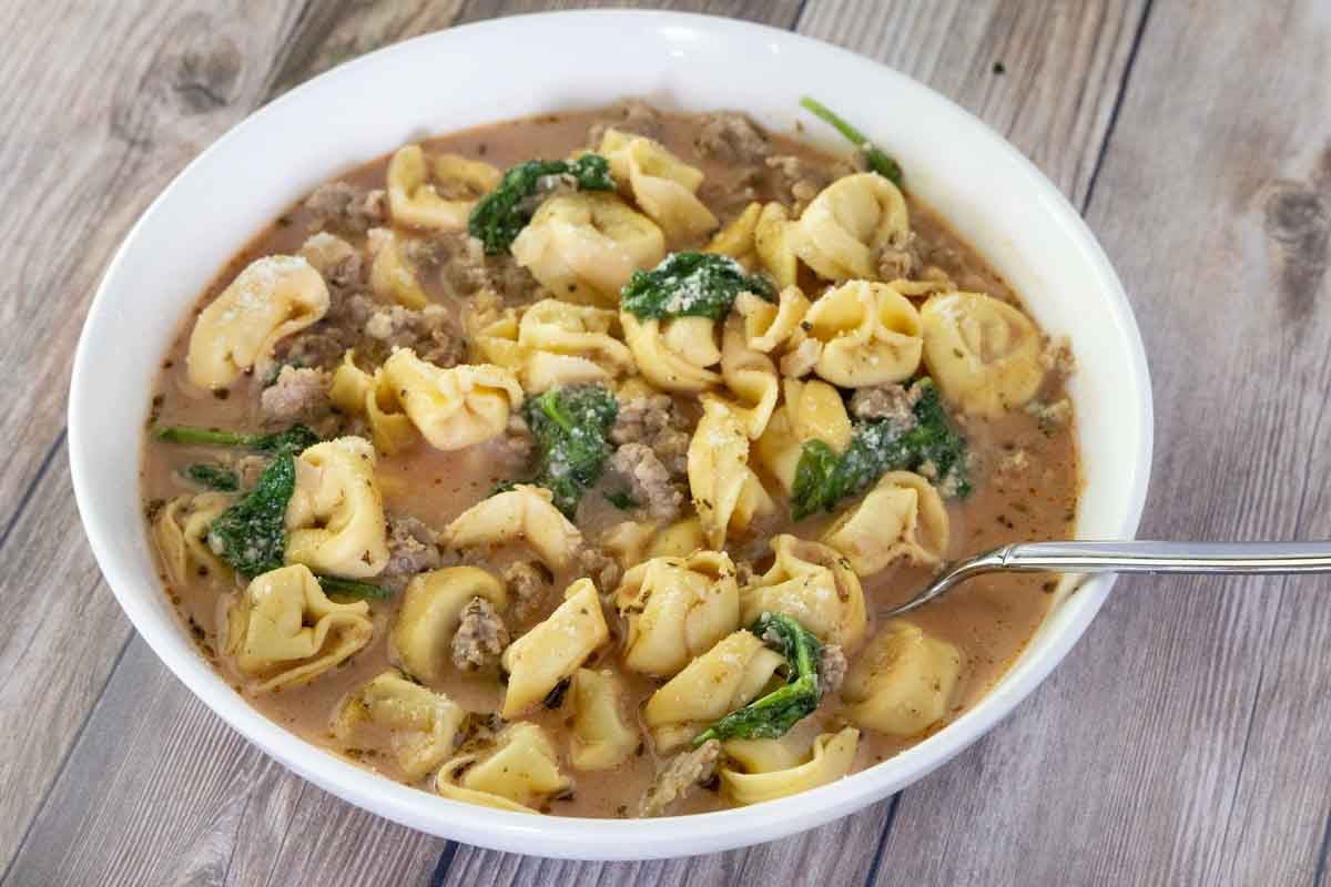 Sausage tortellini soup in a white bowl with a spoon.
