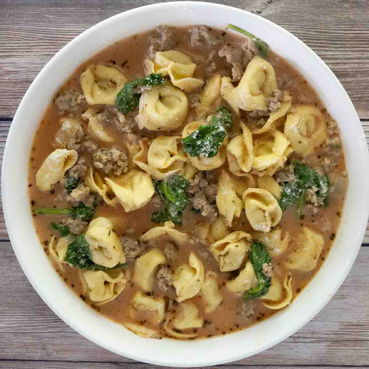 Sausage tortellini soup in a white bowl.