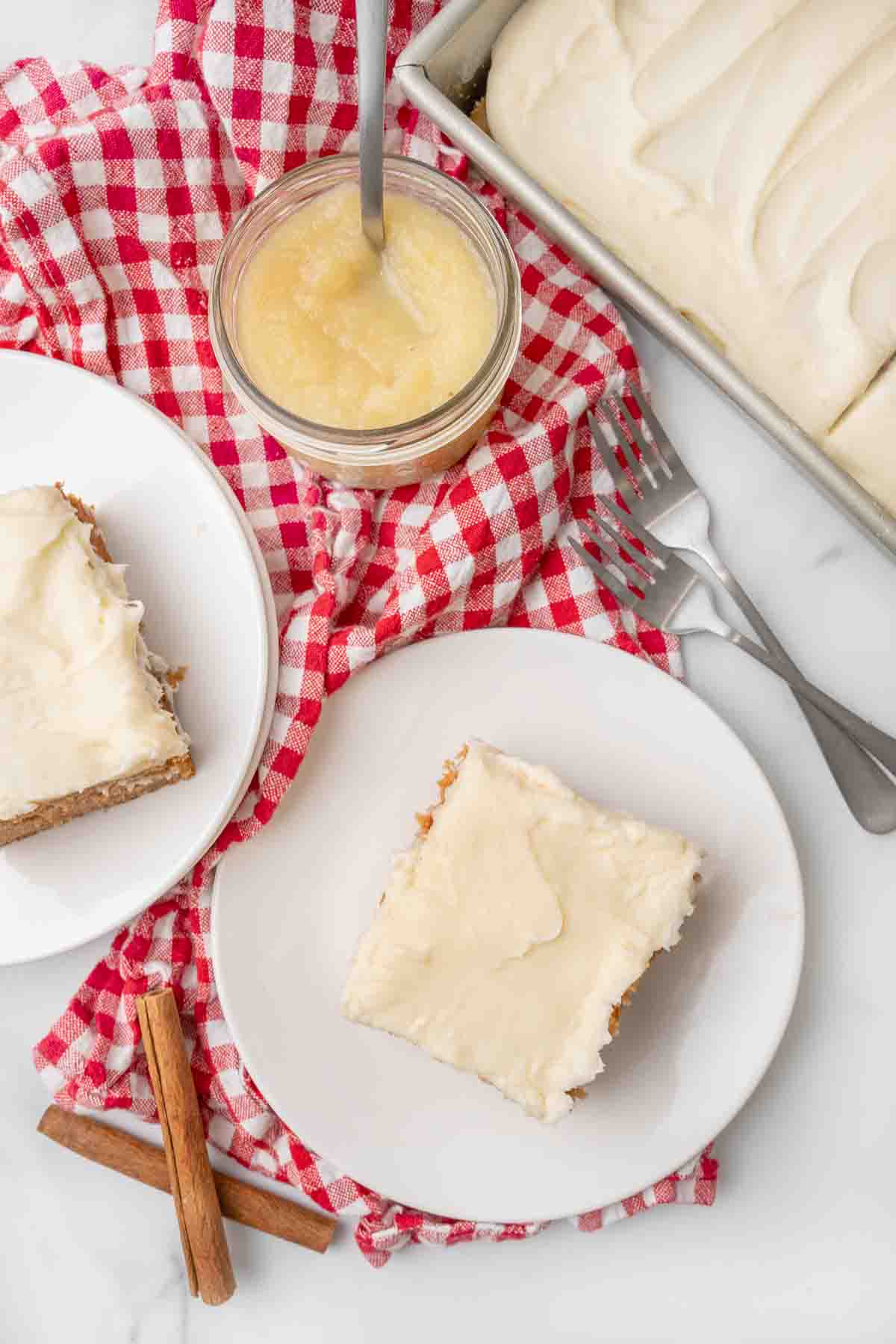 Slices of applesauce cake on white plates with a jar of applesauce.